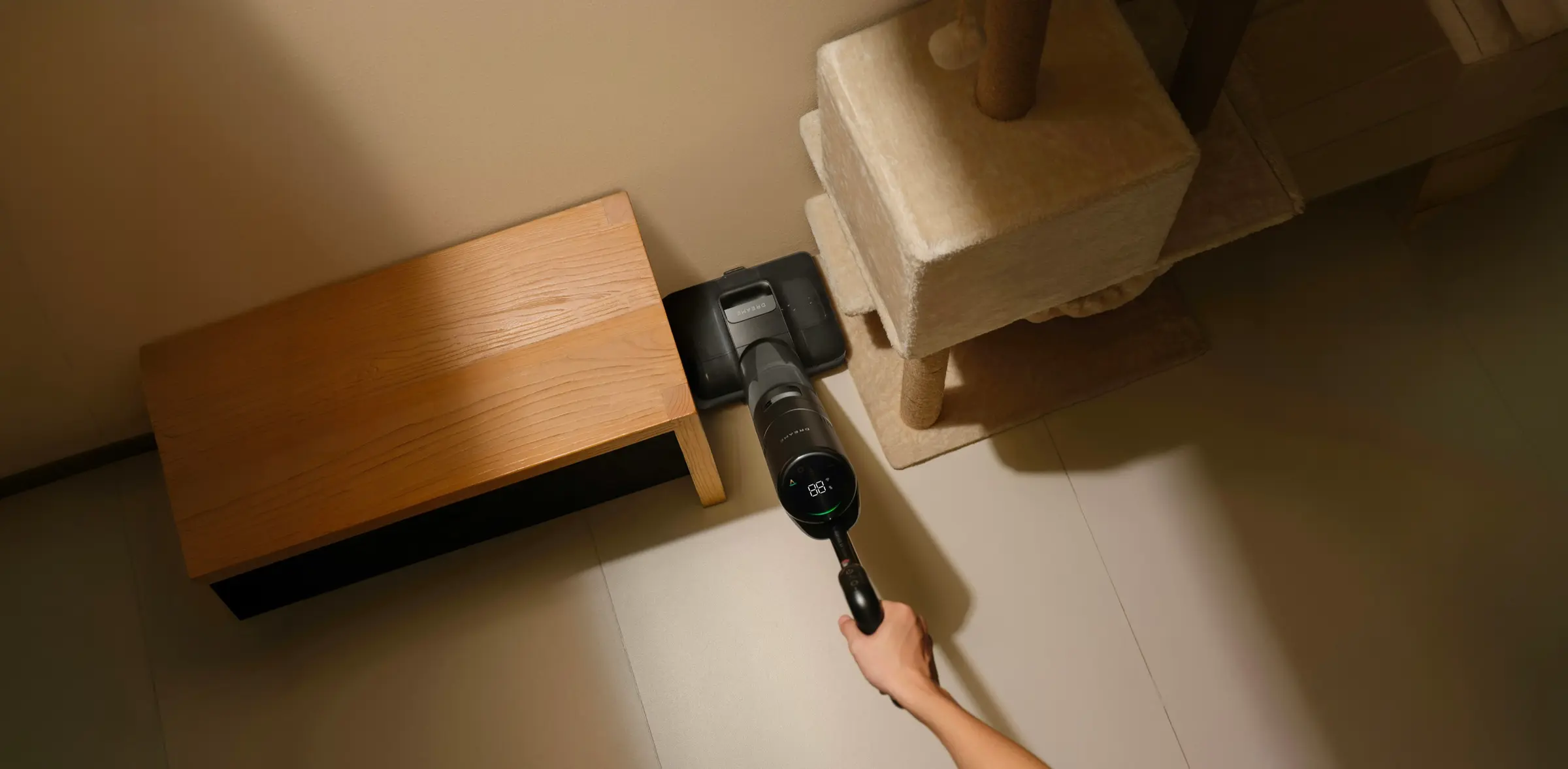 Une main passe un aspirateur balai sous un meuble en bois